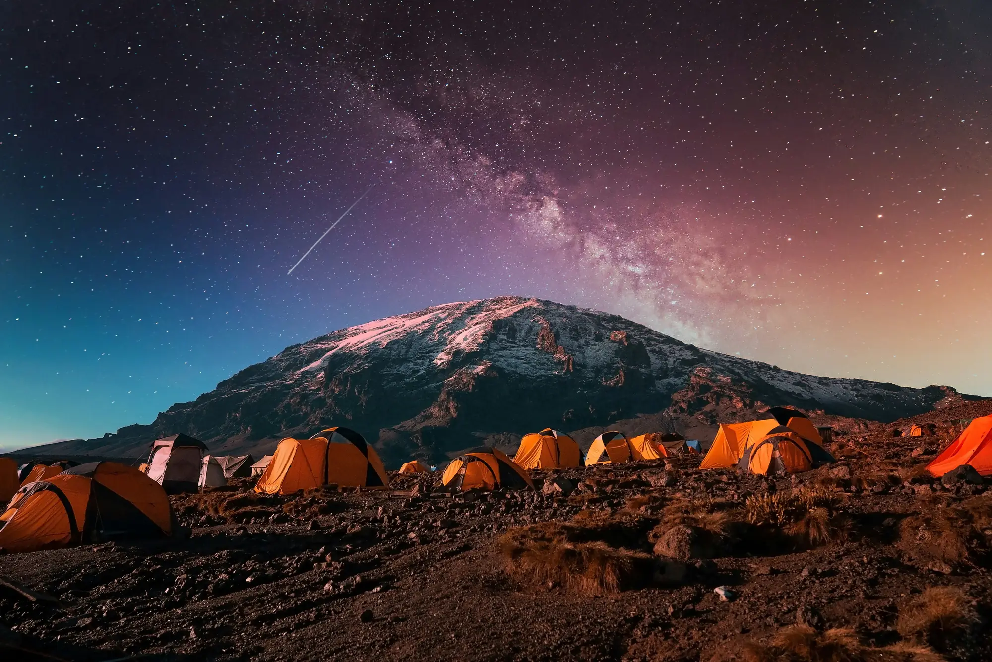 A night view of Kilimanjaro and a set of tents in from of the mountain